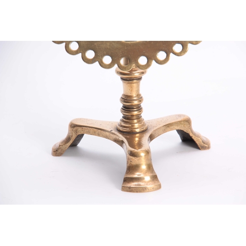 345 - AN 18TH CENTURY BRASS TRIVET with pierced cut out circular tilt-top above a turned stem and tripod b... 