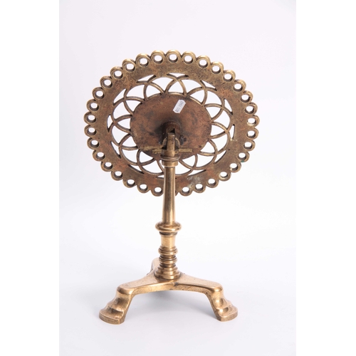 345 - AN 18TH CENTURY BRASS TRIVET with pierced cut out circular tilt-top above a turned stem and tripod b... 