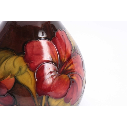 65 - A WALTER MOORCROFT FLAMBE BALUSTER VASE with colourful tube lined Hibiscus flower head and leaf spra... 