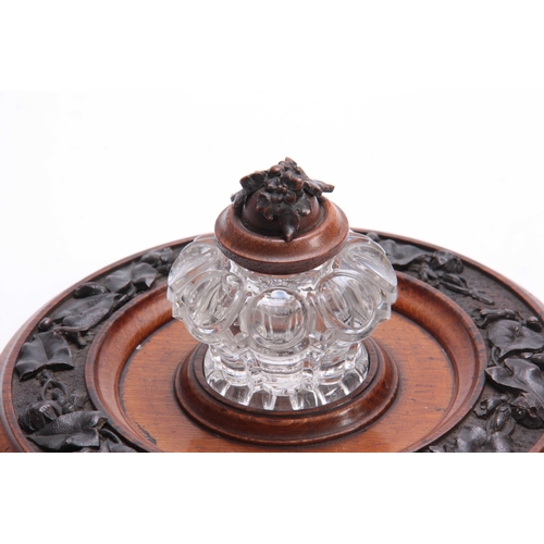 361 - A 19TH CENTURY CARVED OAK CIRCULAR INK STAND with cut glass inkwell to the centre having a floral ca... 