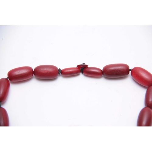 406 - A RED STAINED HORN GRADUATED STRING OF ELONGATED ROUNDED BEADS 64cm overall