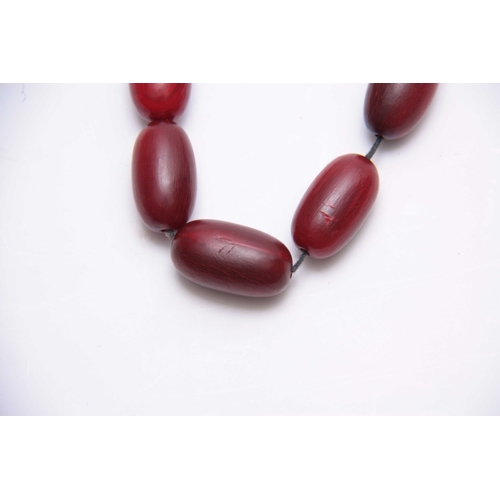 406 - A RED STAINED HORN GRADUATED STRING OF ELONGATED ROUNDED BEADS 64cm overall