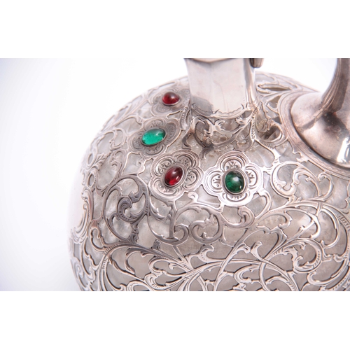 567 - A 19TH CENTURY JEWELLED AND BRIGHT CUT SILVER FILIGREE OVERLAID GLASS CLARET JUG of flattened ovoid ... 