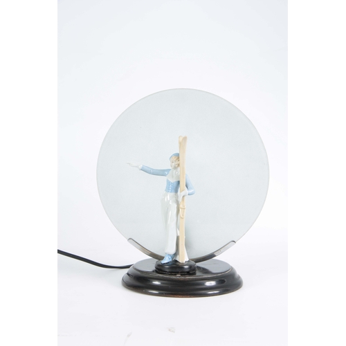 64 - A 1930'S ART DECO CONTINENTAL LAMP mounted with a porcelain figure of a skier having a circular fros... 