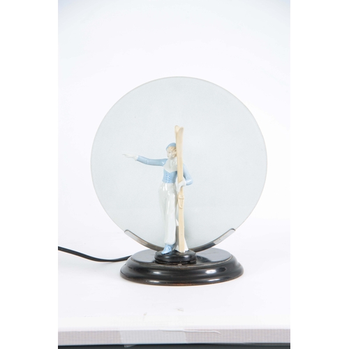 64 - A 1930'S ART DECO CONTINENTAL LAMP mounted with a porcelain figure of a skier having a circular fros... 