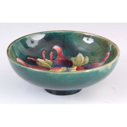 42 - A CIRCA 1950S WALTER MOORCROFT COLUMBINE PATTERN FOOTED BOWL on a green ground 4cm high, 11.5 cm dia... 