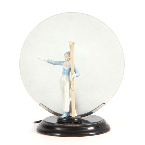 64 - A 1930'S ART DECO CONTINENTAL LAMP mounted with a porcelain figure of a skier having a circular fros... 