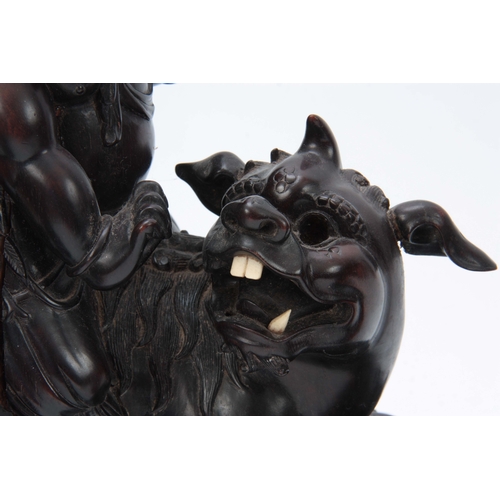 276 - A LATE 19th CENTURY CHINESE HARDWOOD FIGURE RIDING A FOO DOG with glass eyes and bone teeth standing... 