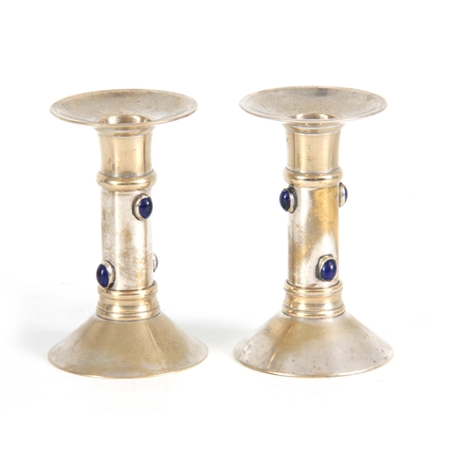 951 - A PAIR OF 20TH CENTURY ARTS AND CRAFTS SILVER PLATED CANDLESTICKS each mounted with 4 blue glass cab... 