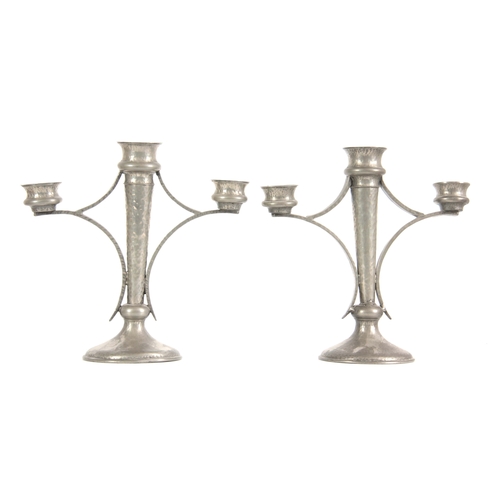 953 - A PAIR OF PEWTER ARTS & CRAFTS CANDELABRA having a hammered finish and tapered stems on circular... 