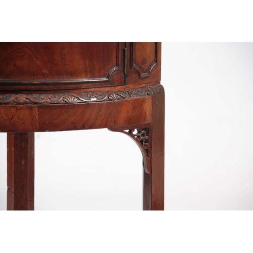 1141 - A GEORGE III MAHOGANY CORNER BEDSIDE TABLE with hinged door above a carved moulded edge, standing on... 