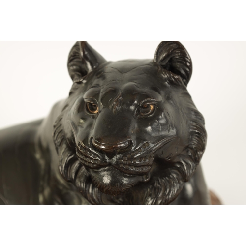 180 - A JAPANESE MEIJI PERIOD PATINATED BRONZE SCULPTURE modelled as a resting tiger on a shaped hardwood ... 