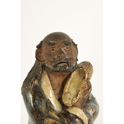 68 - A 19TH CENTURY CHINESE MAJOLICA SLIPWARE FIGURE depiciing an elder holding his slipper. (23cm high )