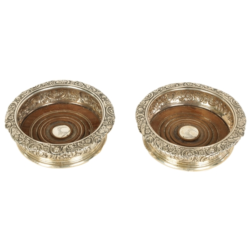 312 - A PAIR OF EARLY 19TH CENTURY SILVER WINE BOTTLE COASTERS with rococo style floral and C scroll embos... 