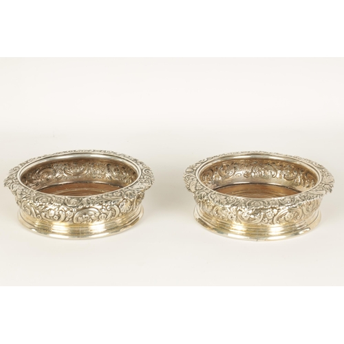 312 - A PAIR OF EARLY 19TH CENTURY SILVER WINE BOTTLE COASTERS with rococo style floral and C scroll embos... 