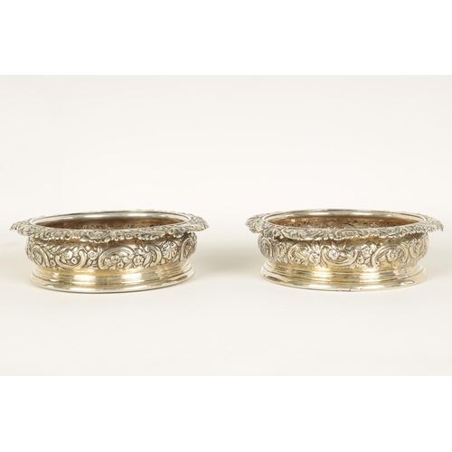 312 - A PAIR OF EARLY 19TH CENTURY SILVER WINE BOTTLE COASTERS with rococo style floral and C scroll embos... 