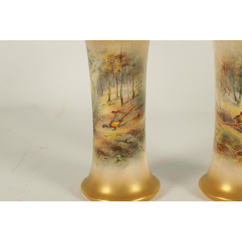 40 - JAMES STINTON. A PAIR OF ROYAL WORCESTER GILT EDGED FLARED CYLINDRICAL CABINET VASES painted with un... 