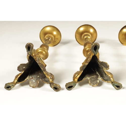 501 - A SET OF FOUR 18TH CENTURY CONTINENTAL LARGE BRASS CANDLESTICKS with cast leaf scrolled tripod bases... 