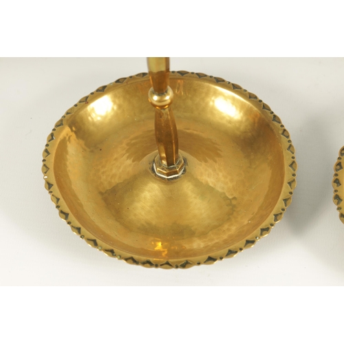 541 - A PAIR OF ARTS AND CRAFTS PLANISHED BRASS CANDLESTICKS the decorated dished bases with knopped facet... 