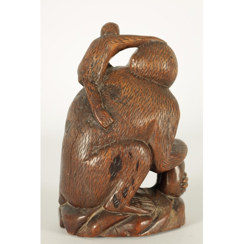 575 - A 19TH CENTURY CARVED HARDWOOD SCULPTURE OF A MONKEY modelled seated clutching a fruit and with infa... 