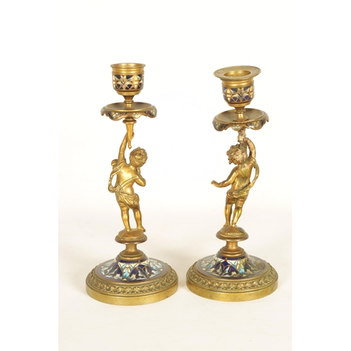 729 - A PAIR OF 19TH CENTURY FRENCH FIGURAL GILT BRONZE AND CHAMPLEVE ENAMEL CANDLESTICKS modelled as two ... 