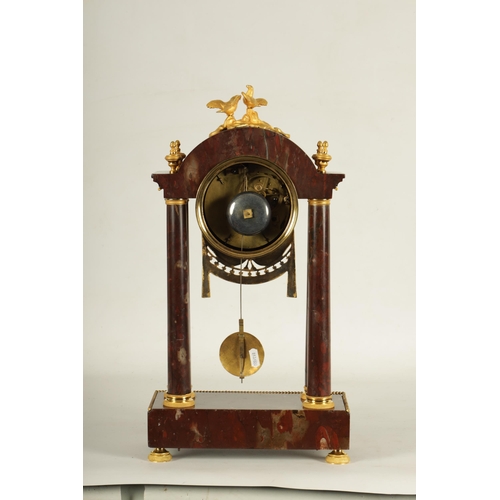 974 - AN EARLY 19TH CENTURY FRENCH ROUGE MARBLE AND ORMOLU PORTICO MANTEL CLOCK the break arched top surmo... 