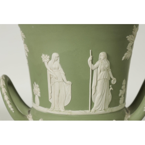 110 - A WEDGWOOD GREEN JASPER WARE TWO-HANDLED URN SHAPED VASE AND COVER ON PEDESTAL BASE decorated with a... 