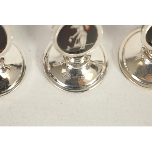 297 - A SET OF FOUR GEORGE V SILVER AND TORTOISESHELL OVAL MENU HOLDERS depicting elegant ladies in fine c... 