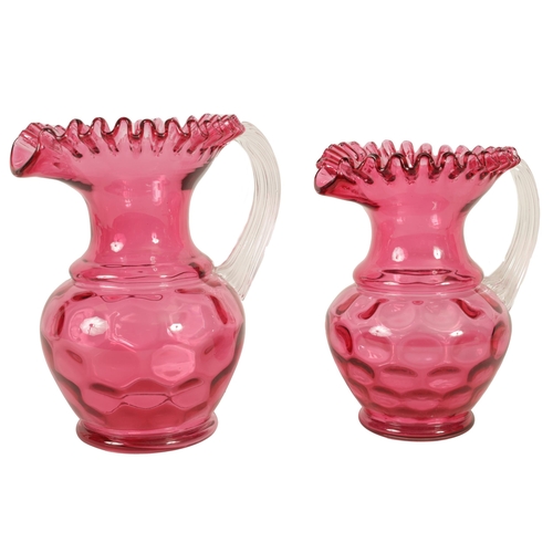 5 - A GRADUATED PAIR OF 19TH CENTURY STYLE OVERSIZED CRANBERRY GLASS JUGS the dimpled bodies beneath wai... 