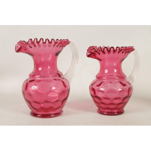 5 - A GRADUATED PAIR OF 19TH CENTURY STYLE OVERSIZED CRANBERRY GLASS JUGS the dimpled bodies beneath wai... 