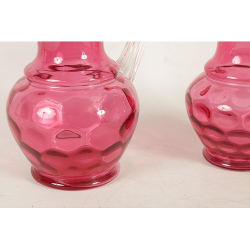 5 - A GRADUATED PAIR OF 19TH CENTURY STYLE OVERSIZED CRANBERRY GLASS JUGS the dimpled bodies beneath wai... 