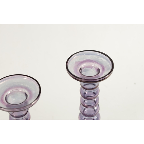 8 - A PAIR OF EARLY 20TH CENTURY IRIDESCENT AUBERGINE GLASS CANDLESTICKS with bobbin type stems and circ... 