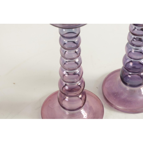 8 - A PAIR OF EARLY 20TH CENTURY IRIDESCENT AUBERGINE GLASS CANDLESTICKS with bobbin type stems and circ... 