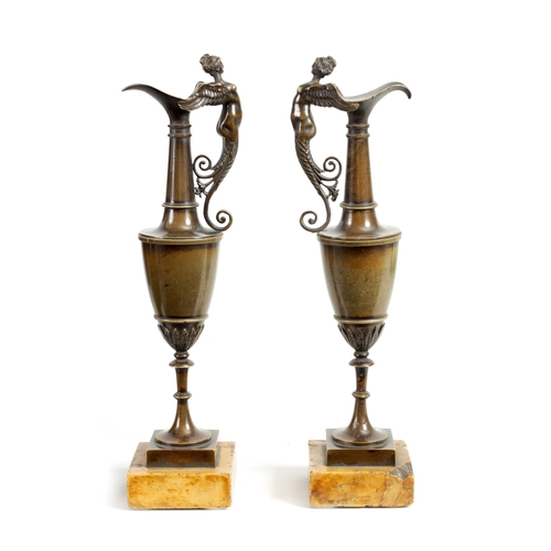 524 - A PAIR OF 19TH CENTURY BRONZE EWERS with figural handles and slender bodies; mounted on square sienn... 