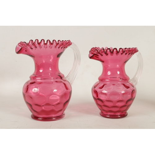 4 - A GRADUATED PAIR OF 19TH CENTURY STYLE OVERSIZED CRANBERRY GLASS JUGS the dimpled bodies beneath wai... 