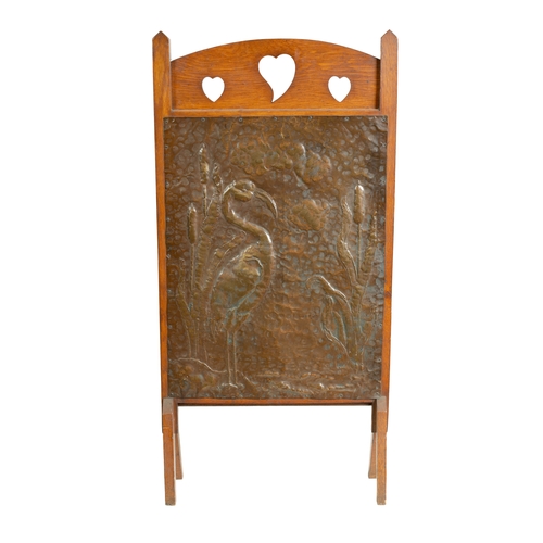 555 - AN ARTS AND CRAFTS PRESSED BRASS AND OAK FIRE SCREEN with pierced love heart decoration and angled f... 