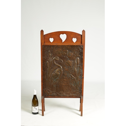 555 - AN ARTS AND CRAFTS PRESSED BRASS AND OAK FIRE SCREEN with pierced love heart decoration and angled f... 