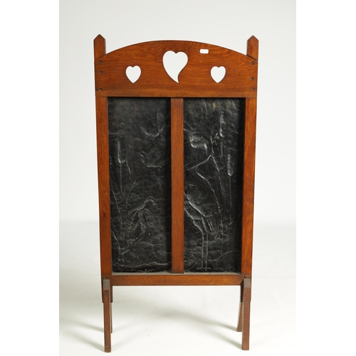 555 - AN ARTS AND CRAFTS PRESSED BRASS AND OAK FIRE SCREEN with pierced love heart decoration and angled f... 