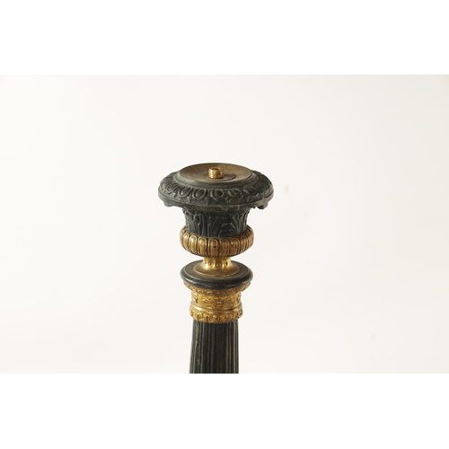 596 - A PAIR OF REGENCY-PATINATED METAL AND BRASS ORMOLU CANDLESTICKS with tapering reeded stems, leaf cas... 