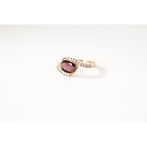 196 - A .375 HALLMARKED YELLOW GOLD AND GARNET SET DRESS RING the oval set stone in a swirled setting with... 