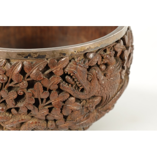 84 - A LATE 19TH CENTURY BURMESE CARVED HARDWOOD SILVER MOUNTED BOWL finely carved with dragons amongst l... 