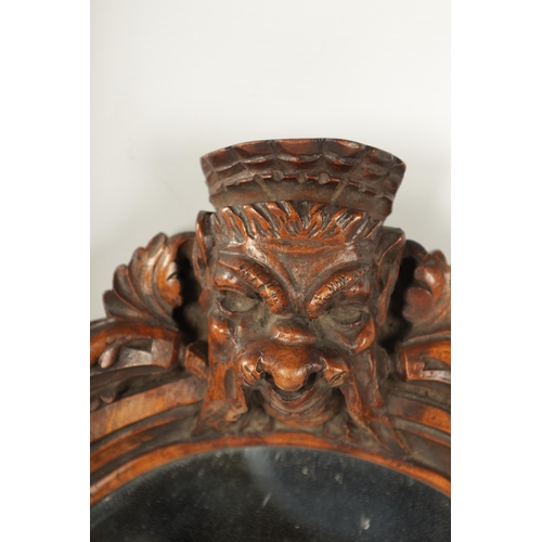 340 - A 19TH CENTURY CARVED WALNUT BLACK FOREST HANGING MIRROR with a monkey head pediment and leaf carved... 