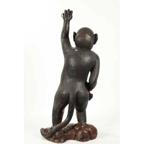 347 - A LIFE SIZE CARVED HARDWOOD SCULPTURE OF A STANDING MONKEY set on a naturalistic base. (145cm high)