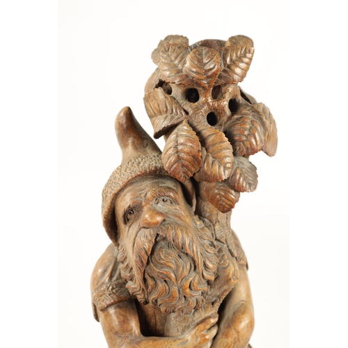 382 - A 19TH CENTURY BLACK FOREST CARVED LINDEN WOOD FIGURE depicting a standing gnome holding a leafing b... 