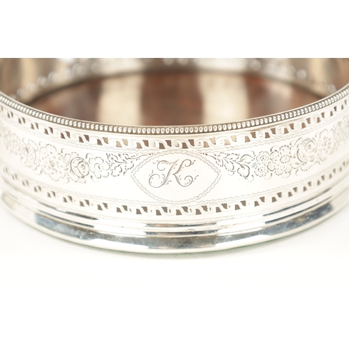 737 - A GEORGE III SILVER BOTTLE COASTER of pierced bright-cut and florally engraved design with hardwood ... 