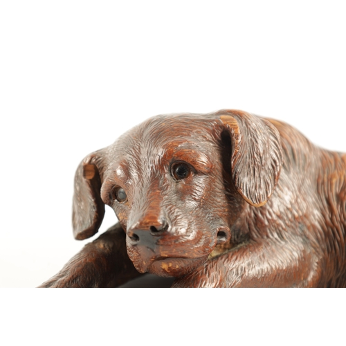 1053 - A 19TH CENTURY BLACK FOREST CARVED LINDEN WOOD DOG SCULPTURE set with glass eyes and seated in a rec... 