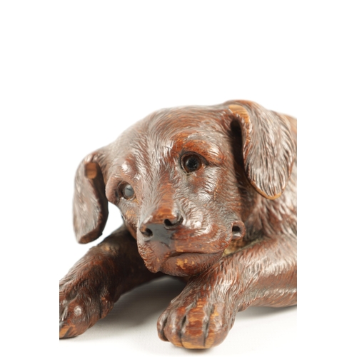 1053 - A 19TH CENTURY BLACK FOREST CARVED LINDEN WOOD DOG SCULPTURE set with glass eyes and seated in a rec... 