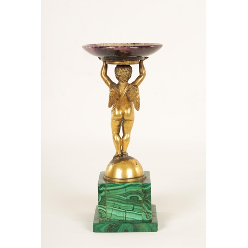 964 - A REGENCY FIGURAL GILT BRONZE, MALACHITE AND BLUE JOHN TAZZA modelled as a gilt bronze winged cherub... 