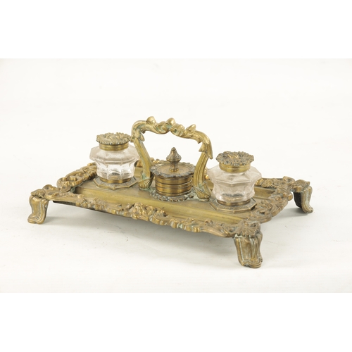 984 - A 19TH CENTURY BRASS ROCOCO INK STAND with glass ink bottles raised on a leaf cast and lions mask ba... 