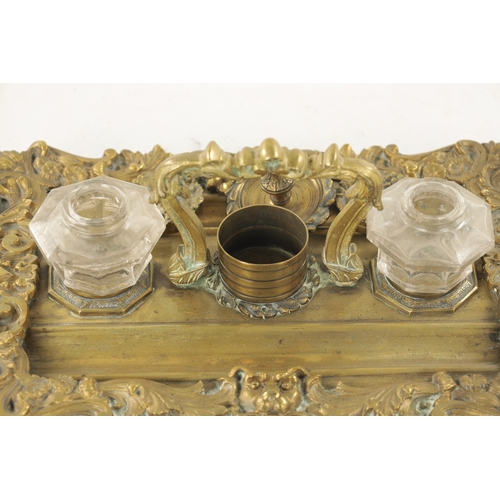 984 - A 19TH CENTURY BRASS ROCOCO INK STAND with glass ink bottles raised on a leaf cast and lions mask ba... 